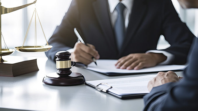 Man in a suit signing documents at a desk with a scale and gavel.